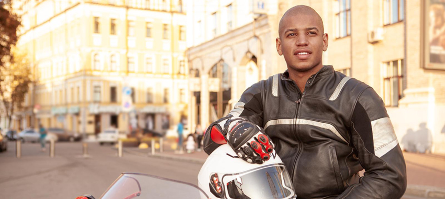 Biker sat on motorcycle holding helmet wearing a new jacket suit.