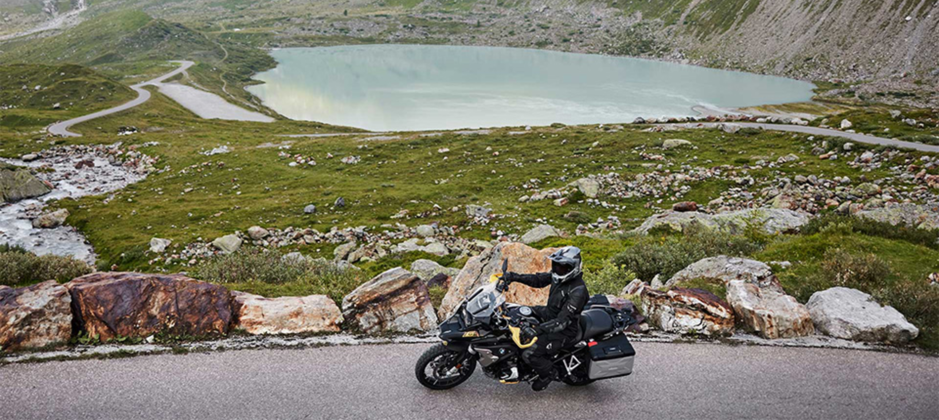 Wide angle view of touring motorcycle travelling across road with lake in background.
