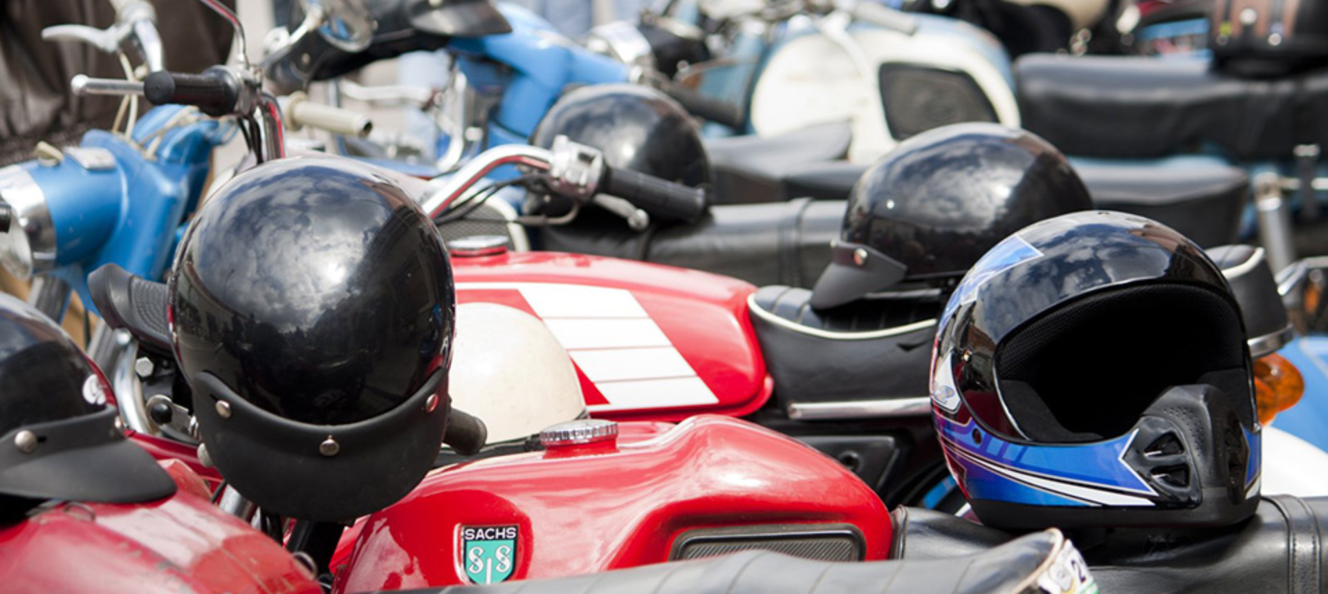Group of motorcycles parked at event with helmets balanced on seats.