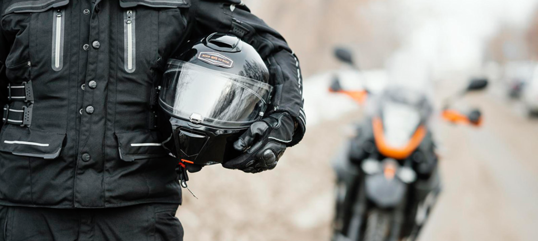 Person holding motorcycle under their arm with motorbike in background.