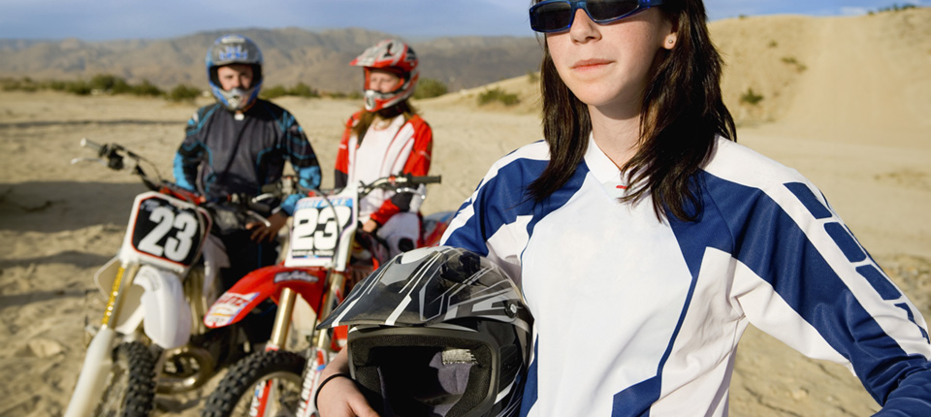 Group of motocross riders sat on bikes whilst holding their helmets.