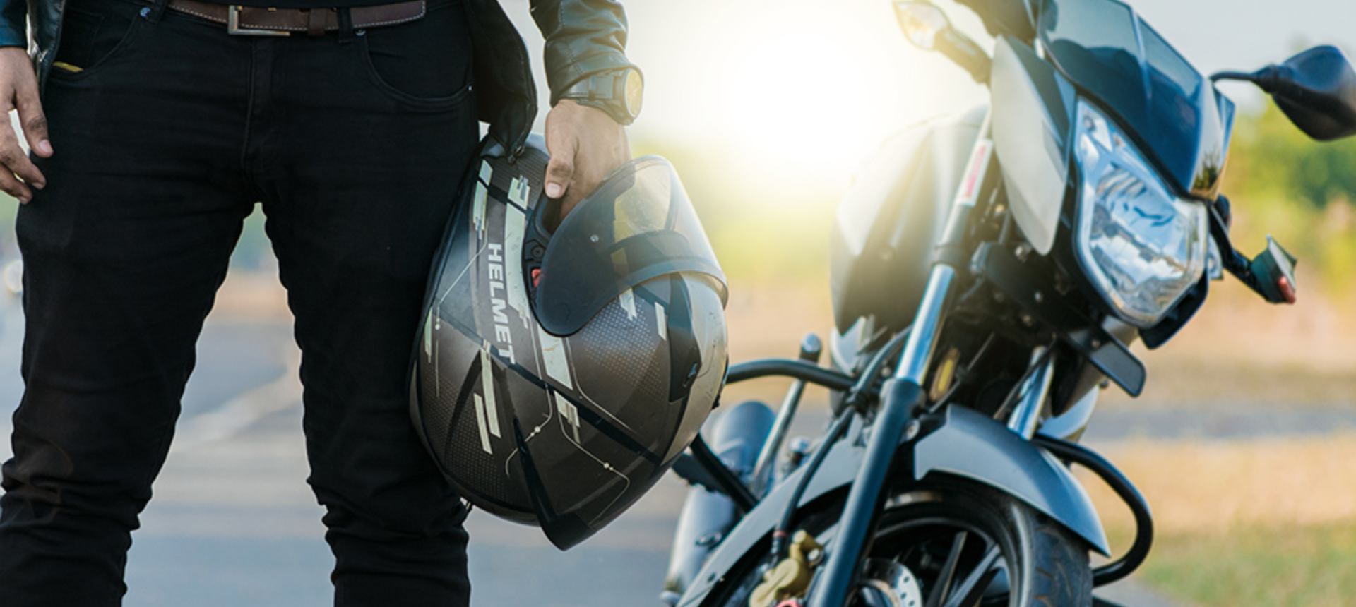 Man stood with motorcycle helmet in his hand in front of motorbike.