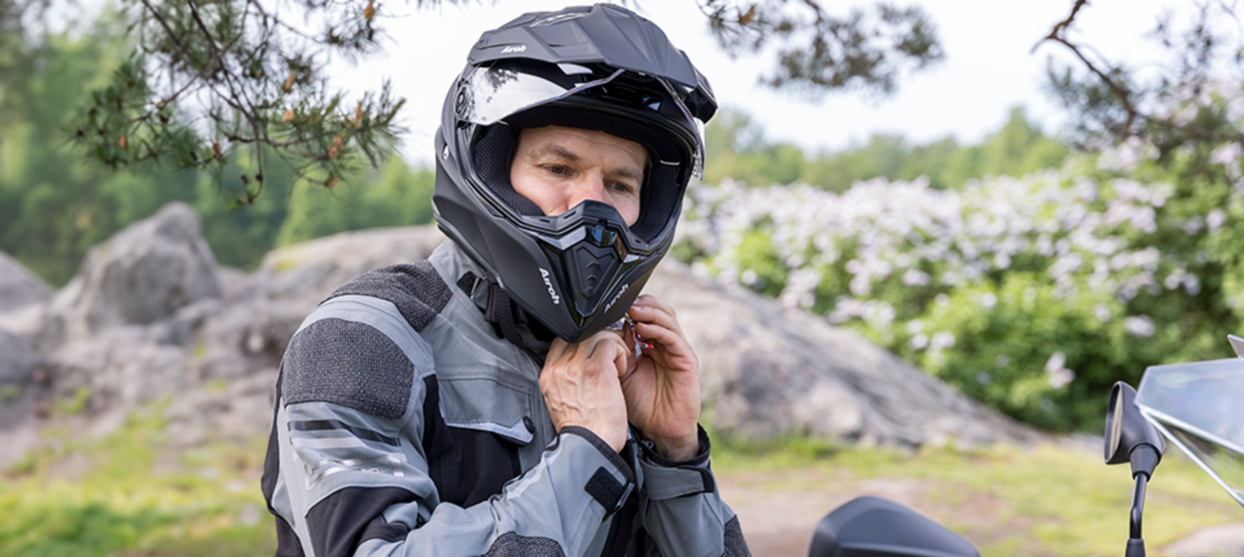 Man attaching chin strap on their helmet whilst sat on motorcycle.