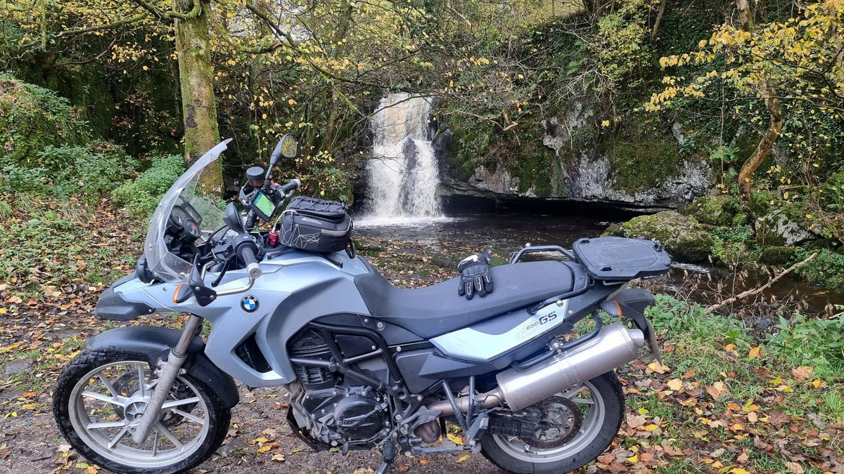 BMW motorcycle parked beside a woodland waterfall during an autumn ride in the UK.
