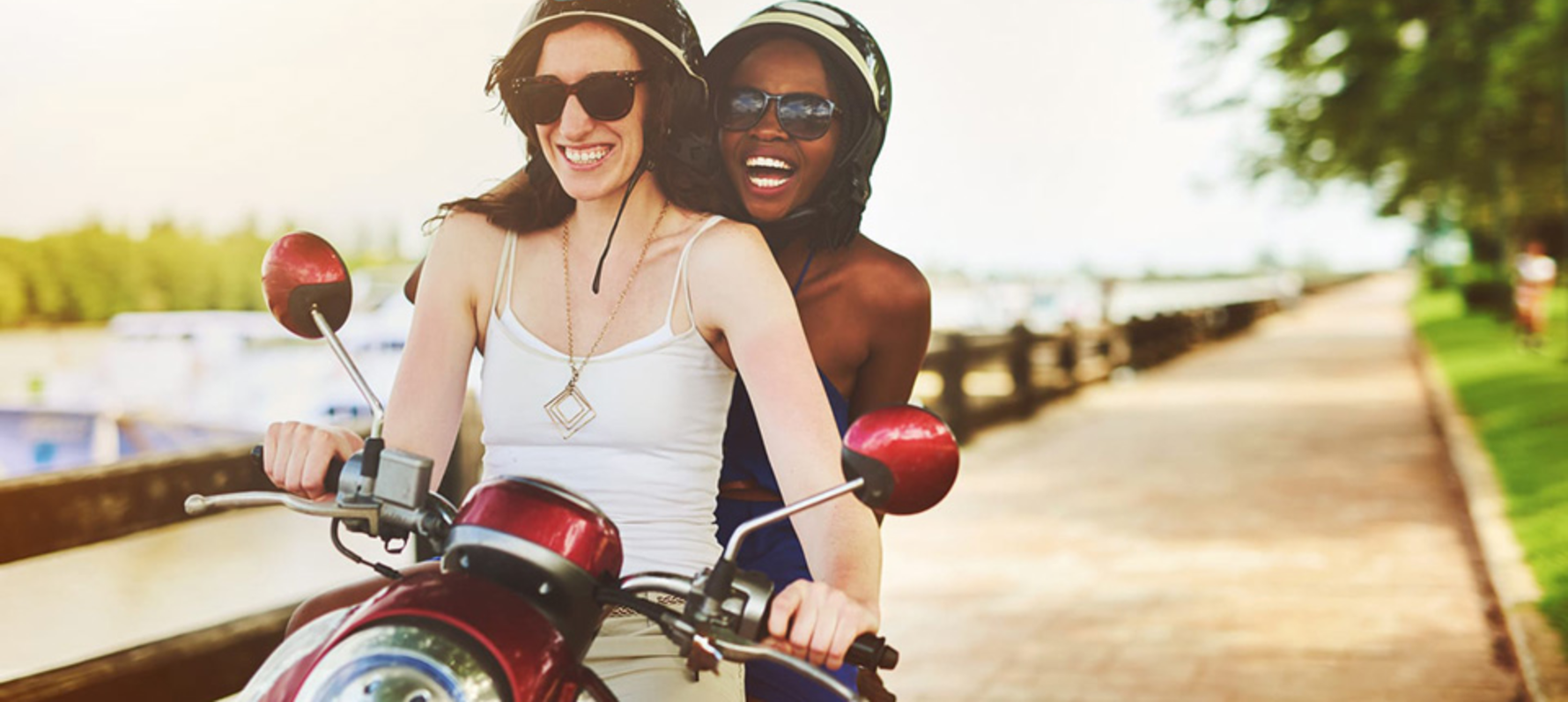 Two women on a scooter wearing a helmet and vest tops. 