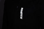 Close-up of a black zippered bowtex jacket with a vertical reflective 'ROWTEX' logo printed on the chest. picture aken in the dark