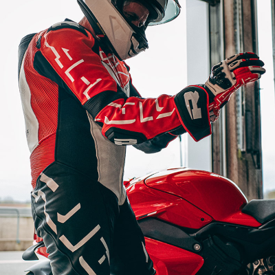 Motorcyclist stood next to motorbike in full leather suit putting on gloves.