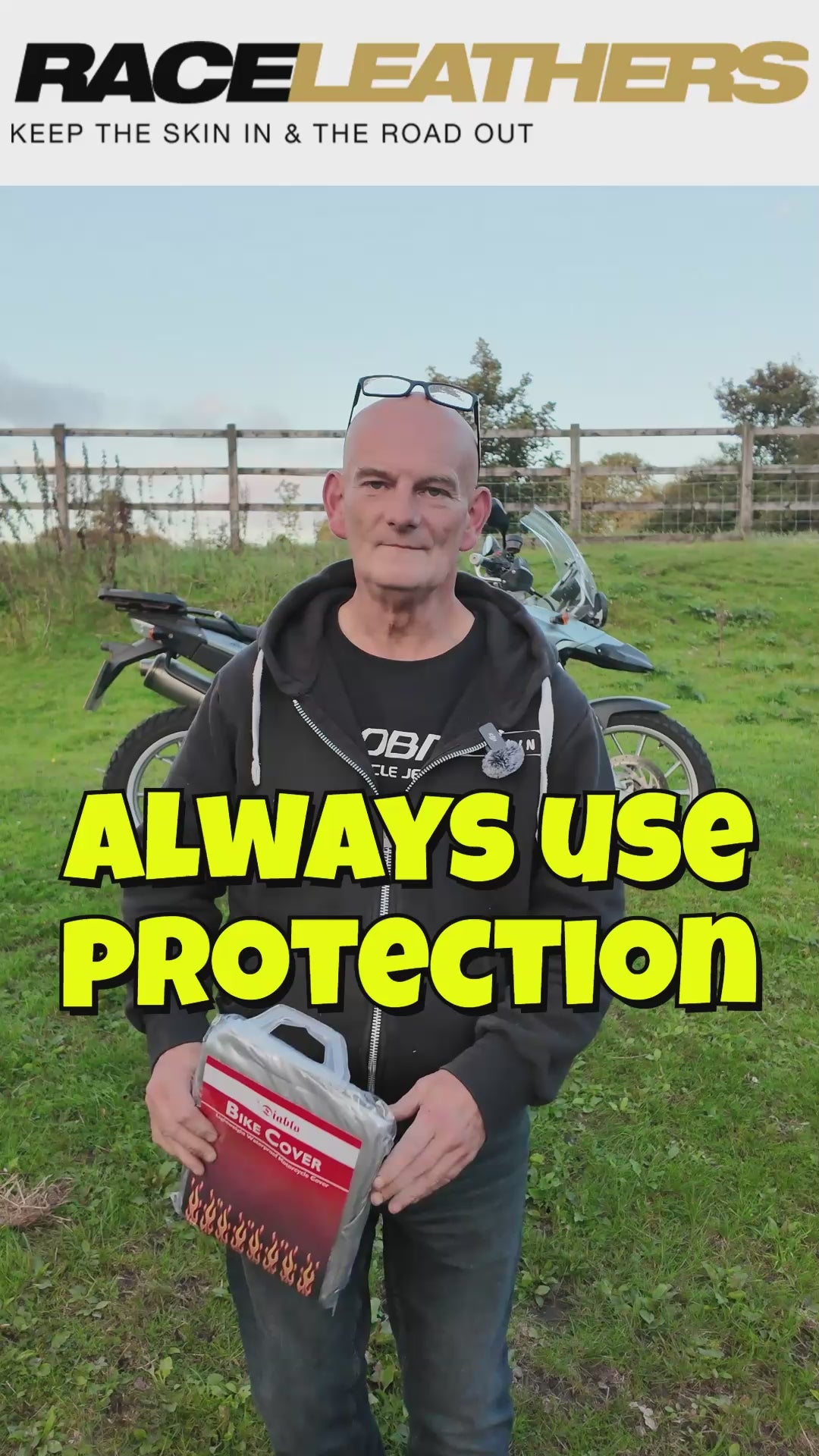 Keith at Raceeathers Demonstrating The DIABLO Motorcycle Raincover in a field, in front of a wooden fence with a blue sky.