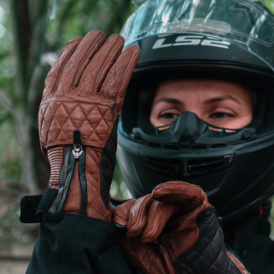 Woman wearing a helmet whilst putting on motorcycle gloves.